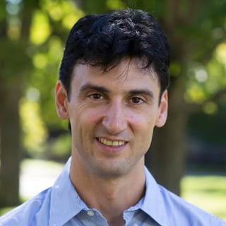 Itai Yanai smiling in a light blue button-up shirt outdoors with blurred green trees in the background