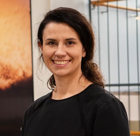 Woman with long dark hair wearing a black shirt smiles at the camera indoors