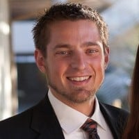 Professional headshot of a smiling man in a business suit and tie against a blurred background